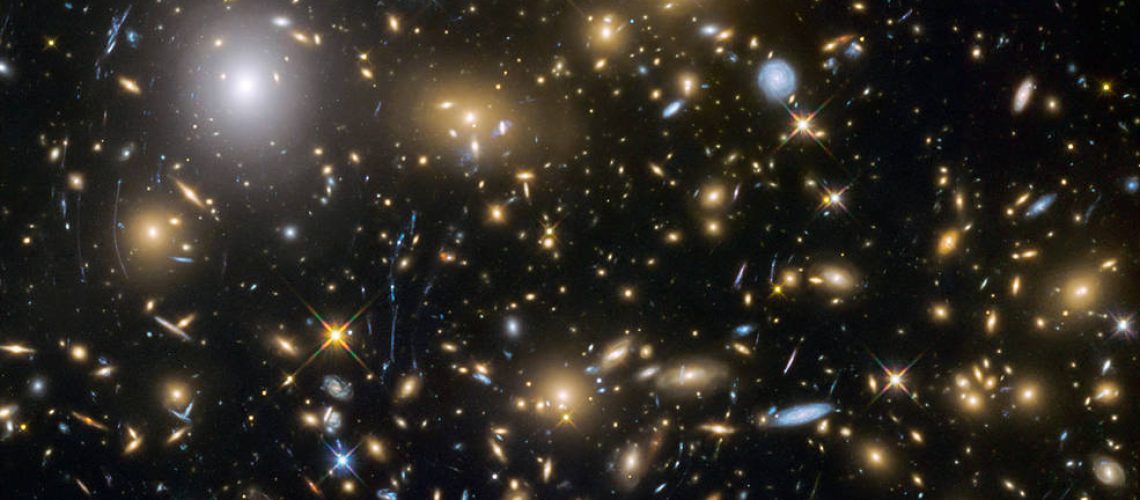 This image from the NASA/ESA Hubble Space Telescope shows the galaxy cluster MACSJ0717.5+3745. This is one of six being studied by the Hubble Frontier Fields programme, which together have produced the deepest images of gravitational lensing ever made. Due to the huge mass of the cluster it is bending the light of background objects, acting as a magnifying lens. It is one of the most massive galaxy clusters known, and it is also the largest known gravitational lens. Of all of the galaxy clusters known and measured, MACS J0717 lenses the largest area of the sky.